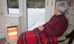 Donna anziana con una coperta sulle gambe e una stufetta accesa davanti
