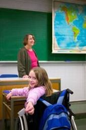 Bimba con disabilità davanti a insegnante, si gira verso l'obiettivo fotografico