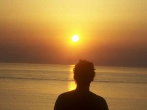 Ombra di giovane uomo fotografat di spalle, di fronte a un sole che nasce