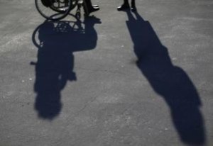 Particolare di persona in carrozzina e di persona non disabile e le loro ombre sull'asfalto