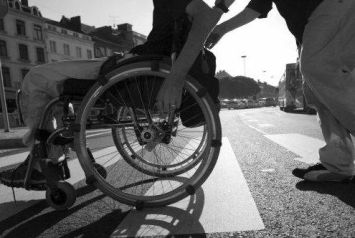 Particolare di persona in carrozzina spinta sulle strisce da una persona non disabile