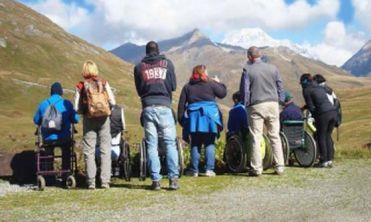 Fotografia di varie persone con disabilità, con accompagnatori, davanti a delle montagne