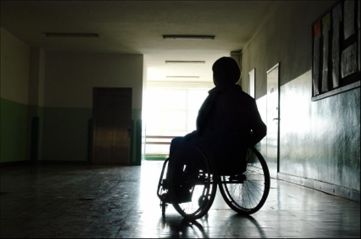 Persona in carrozzina in ombra, nel locale di un ospedale