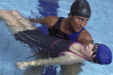 Donna in piscina sorregge un bambino con disabilità