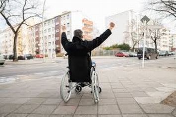 Uomo con disabilità in carrozzina fotografato di spalle con le braccia levate
