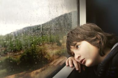 Bambino di fronte a una finestra con gocce di pioggia sul vetro