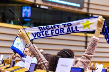 Persona con disabilità al Parlamento Europeo con una sciarpa recante la scritta "Right to Vote for all"