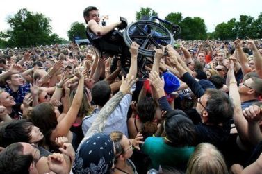 Giovane in carrozzina sollevato in alto da tante persone a un concerto dal vivo