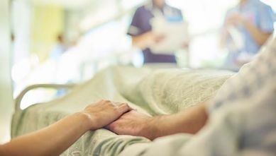 Mano di una caregiver tiene la mano di una persona in un letto di ospedale