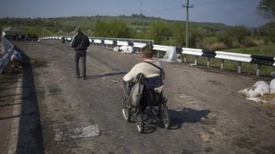 Persona con disabilità in carrozzina attraversa un ponte in piena zona di guerra in in Ucraina (©Alexander Zemlianichenko/AP)