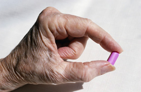 Mano di persona anziana con una pillola tra le dita