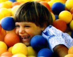 Bambino che gioca in mezzo a tante palline colorate