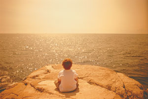 Bimbo fotograftao di spalle su una roccia che guarda il sole che nasce sul mare