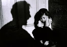 Fotografia in bianco e nero di bambina con le mani sulle orecchie, con un adulto in ombra che urla in primo piano