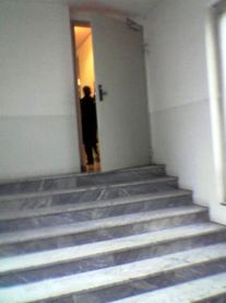 Porta socchiusa, con una persona dietro, in cima a una scalinata
