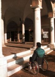 Uomo con disabilità davanti a un colonnato cui non può accedere a causa di tre gradini