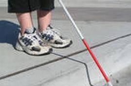 Particolare di bimbo cieco col bastone bianco, sul bordo di un marciapiede