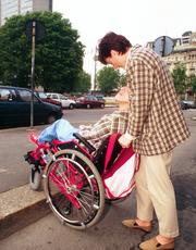 Persona con grave disabilità in carrozzina, spinta da accompagnatrice