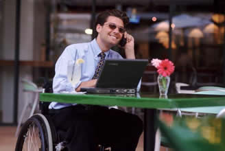 Persona in carrozzina parla al telefono e lavora al computer portatile