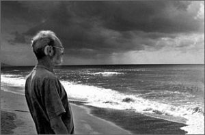 Foto in bianco e nero di una persona con gli occhiali sulla riva del mare che guarda un temporale all'orizzonte