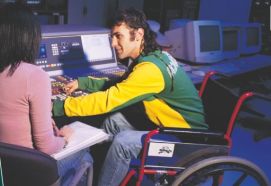 Giovane con disabilità al lavoro al computer insieme a donna non disabile vista di spalle