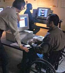 Uomo in carrozzina lavora al computer. Vicina una donna non disabile