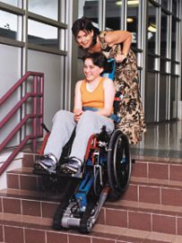 Bimba in carrozzina sulle scale di una scuola, con un ausilio che ne aiuta il movimento