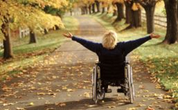 Donna con disabilità fotografata di spalle sul viale di un parco, con le braccia sollevate