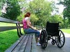 Donna con disabilità seduta su una panchina. Al suo fianco una carrozzina