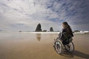 Giovane donna in carrozzina di fronte a una spiaggia e a due grandi rocce