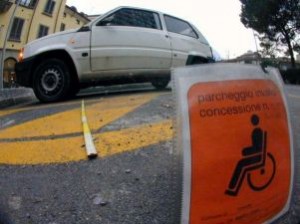 In primo piano contrassegno, dietro un parcheggio per disabili