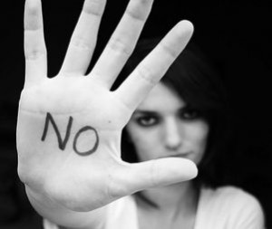Primo piano di mano di donna, con la scritta "No" sul palmo. Sullo sfondo il viso