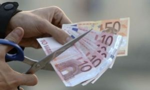 Mano che taglia delle banconote di euro con una forbice