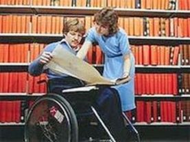 Uomo con disabilità esamina dei documenti in biblioteca, insieme a una donna