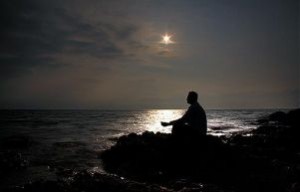 Uomo che guarda il cielo notturno e la luna, seduto su uno scoglio