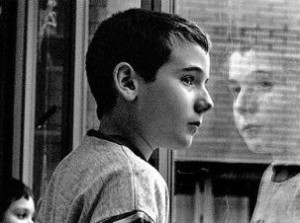 Foto in bianco e nero di profilo di ragazzo davanti a un vetro che riflette la sua immagine