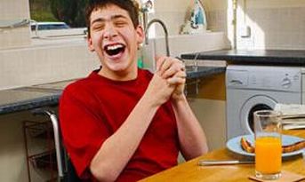 Giovane con disabilità che ride, seduto presso un tavolo di cucina