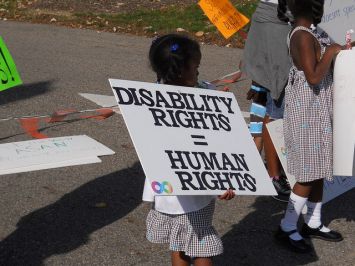Bimba con cartello in mano ove è scritto: "Disability Rights = Human Rights"