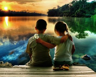 Un ragazzo e una ragazza fotografati di spalle davanti a un lago al tramonto