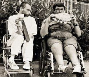 Un giovane con distrofia che mangia un enorme panino e un altro che beve (foto di Archivio UILDM Bergamo)i