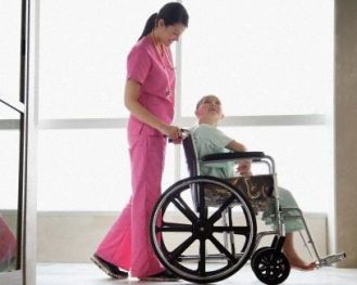 Ragazzo con disabilità in carrozzina, in un corridioi di ospedale con un'assistente