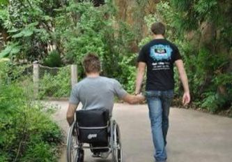 Uomo in carrozzina a mano di un uomo senza disabilità (fotografati di spalle)