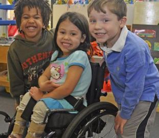 Due bambini senza disabilità e una bambina con disabilità in carrozzina