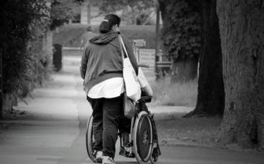 Persona di spalle che spinge una persona con disabilità in carrozzina