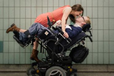 Giovane donna non disabile bacia un uomo con disabilità in carrozzina
