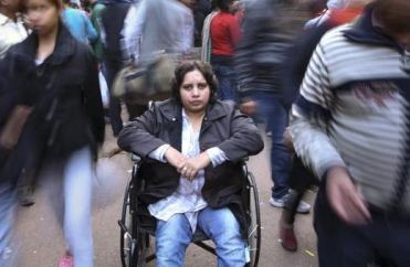 Donna con disabilità in carrozzina al centro di altre figure sfuocate