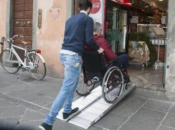 Persona con disabilità in carrozzina che entra in un negozio grazie a una pedana