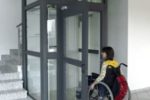 Una persona con disabilità in carrozzina davanti a un ascensore condominiale