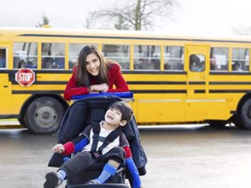 Bimbo con disabilità insieme a ragazza senza disabilità, davanti a un mezzo per il trasporto scolastico