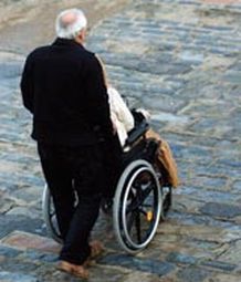 Persona anziana spinge la carrozzina di una persona con disabilità
